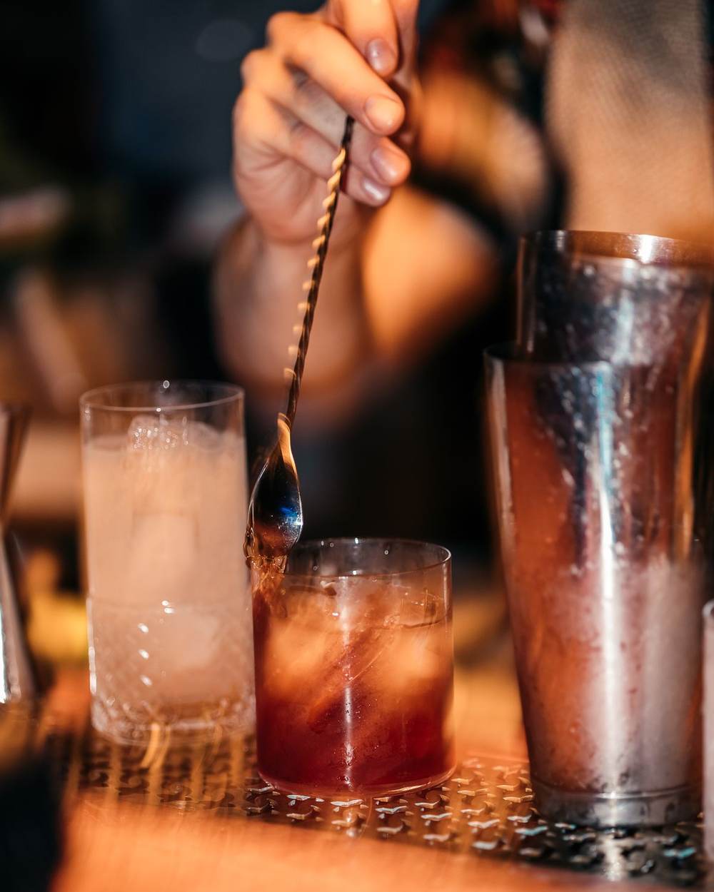 Bartender hand stirring a cocktail in a dimly lit bar