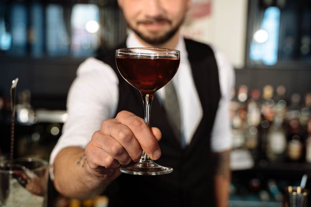 Close-up bartender handing a cocktail across a bar